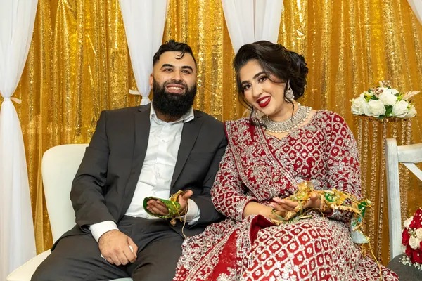 Bride in a red and gold lehenga and groom seated together, smiling